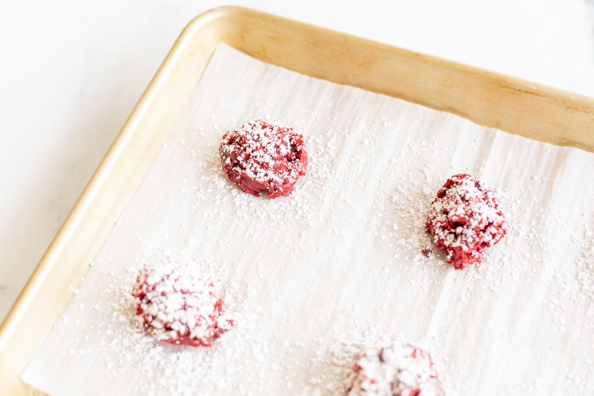 Red velvet gooey butter cookies dusted in powder sugar on a gold baking sheet.