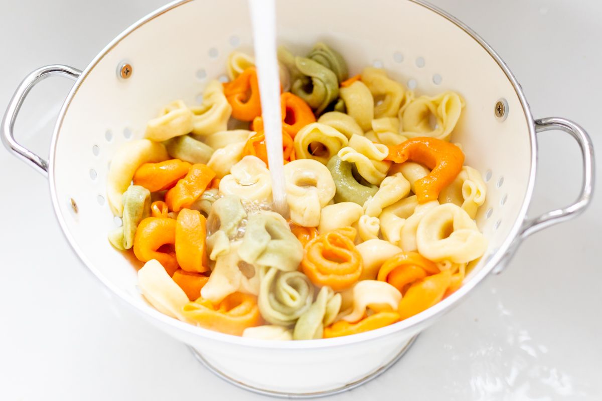 Tortellini pasta in a white colander in a sink.