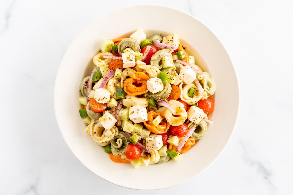 A white serving bowl full of tortellini pasta salad.