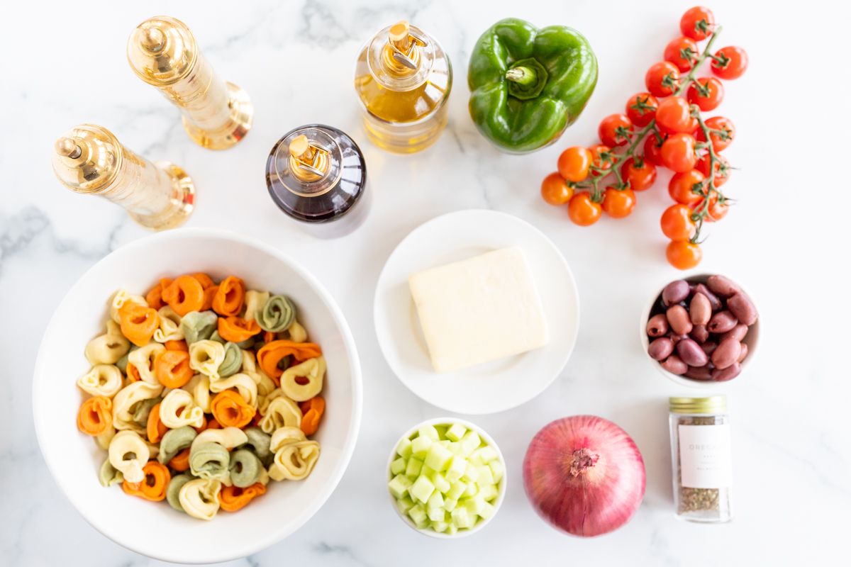 Ingredients for tortellini pasta salad spread out on a marble countertop.