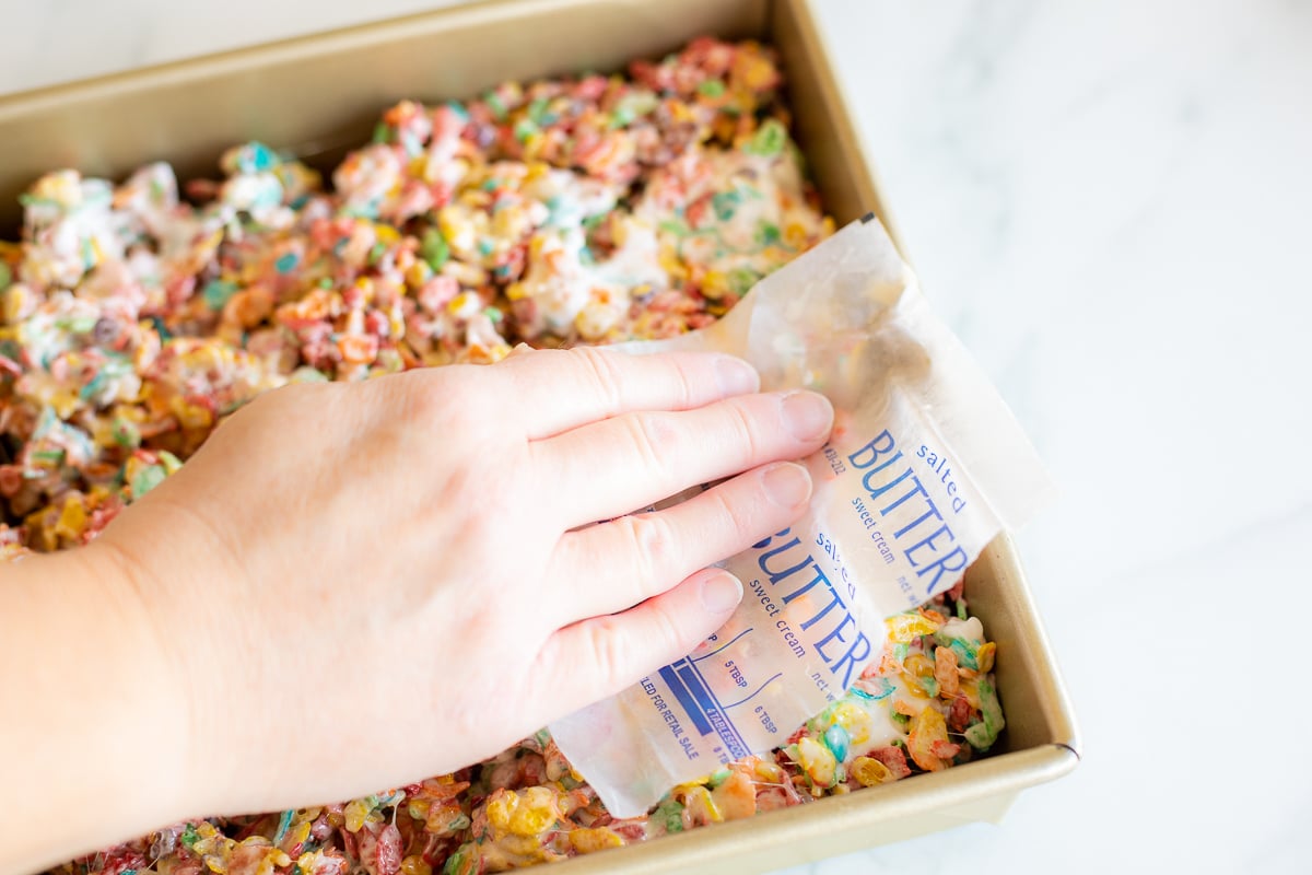 Hand using butter wrapper to gently press down Fruity Pebbles Treats