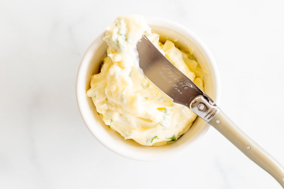 Overhead view of garlic butter in small bowl with butter spreader