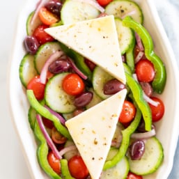 Overhead view of Greek salad on platter with two wedges of feta set over the top