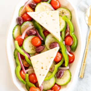 Overhead view of Greek salad on platter with two wedges of feta set over the top