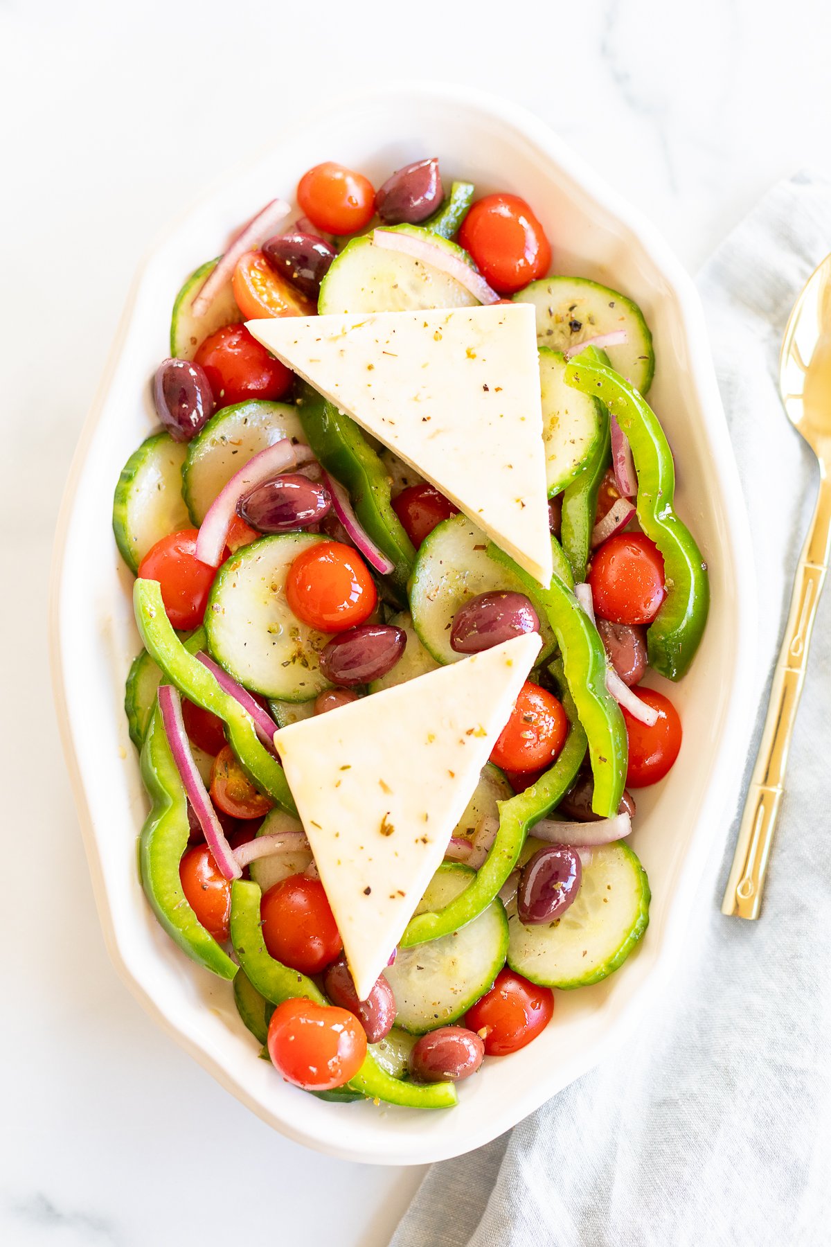 Overhead view of Greek salad on platter with two wedges of feta set over the top