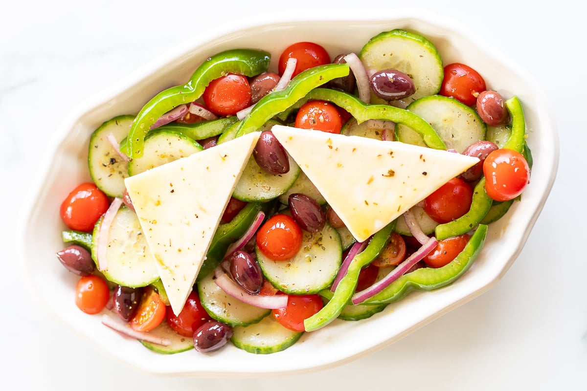 Overhead view of Greek salad on platter with two wedges of feta set over the top