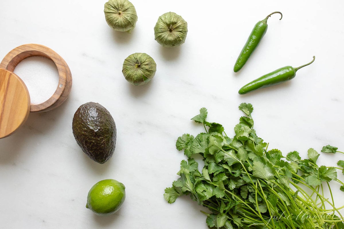 Jalapenos, tomatillos, cilantro and avocado on a white countertop.