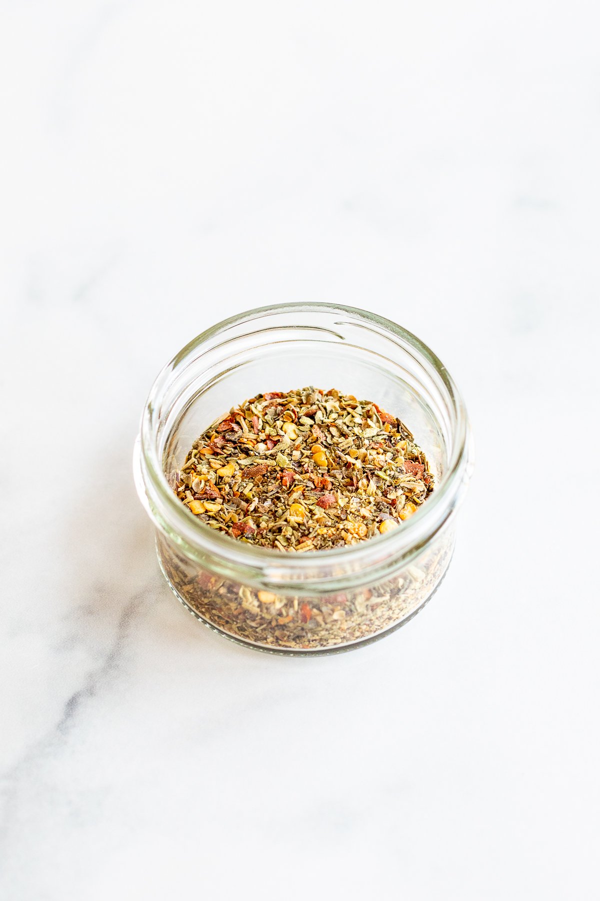 Jar of oregano seasoning on marble countertop