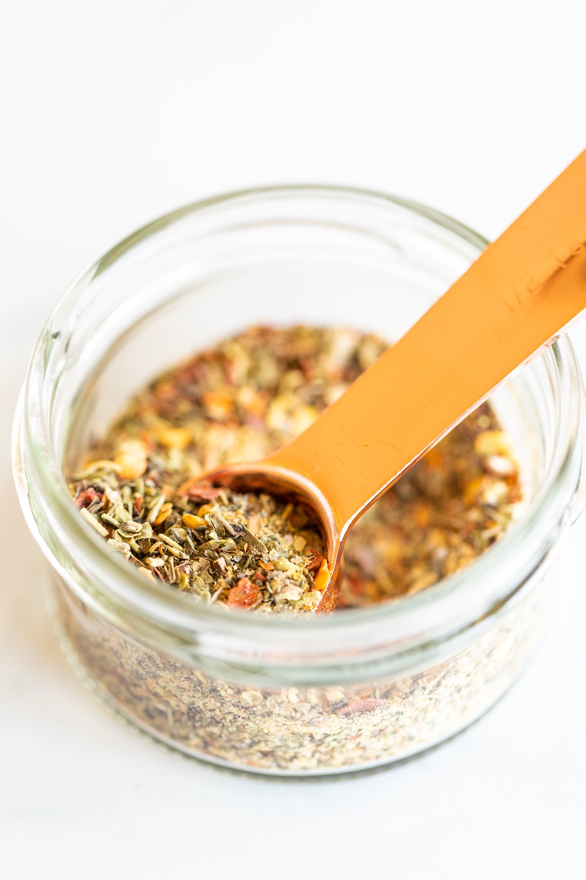 Measuring spoon scooping oregano seasoning from jar