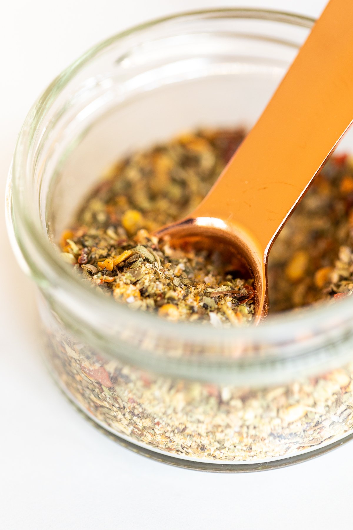 Measuring spoon scooping oregano seasoning from jar