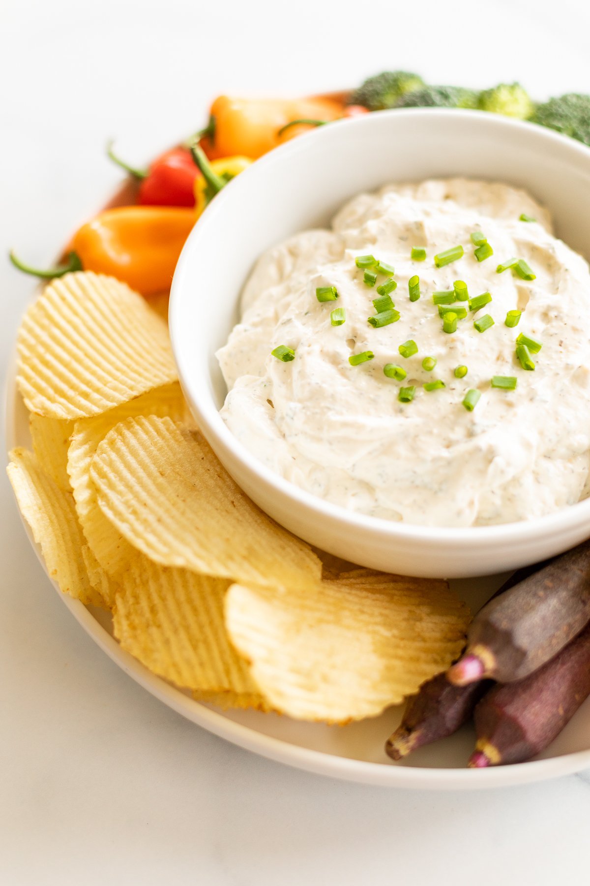 Bowl of ranch dip garnished with fresh chives, set on platter with chips and veggies