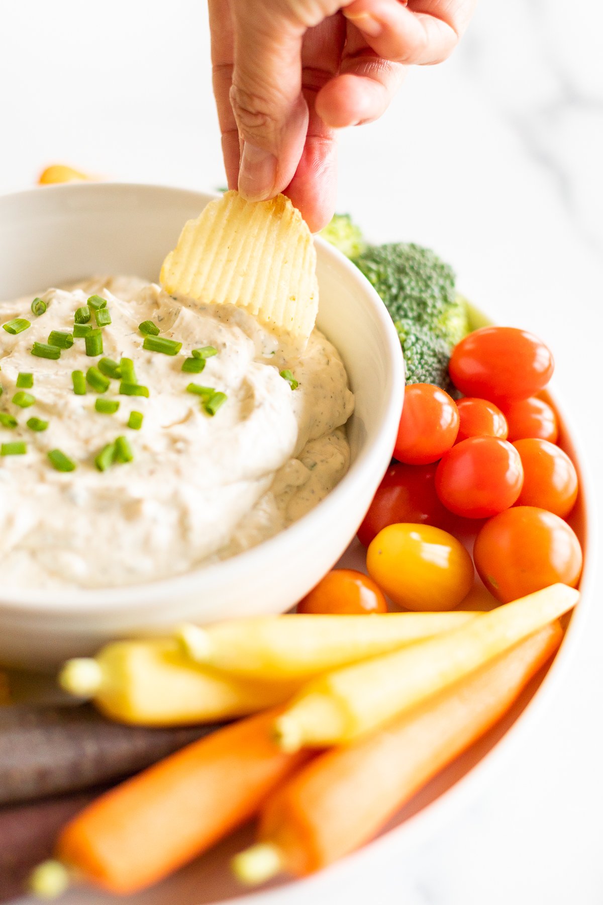 Dipping ridged potato chip into ranch dip set on serving platter with veggies