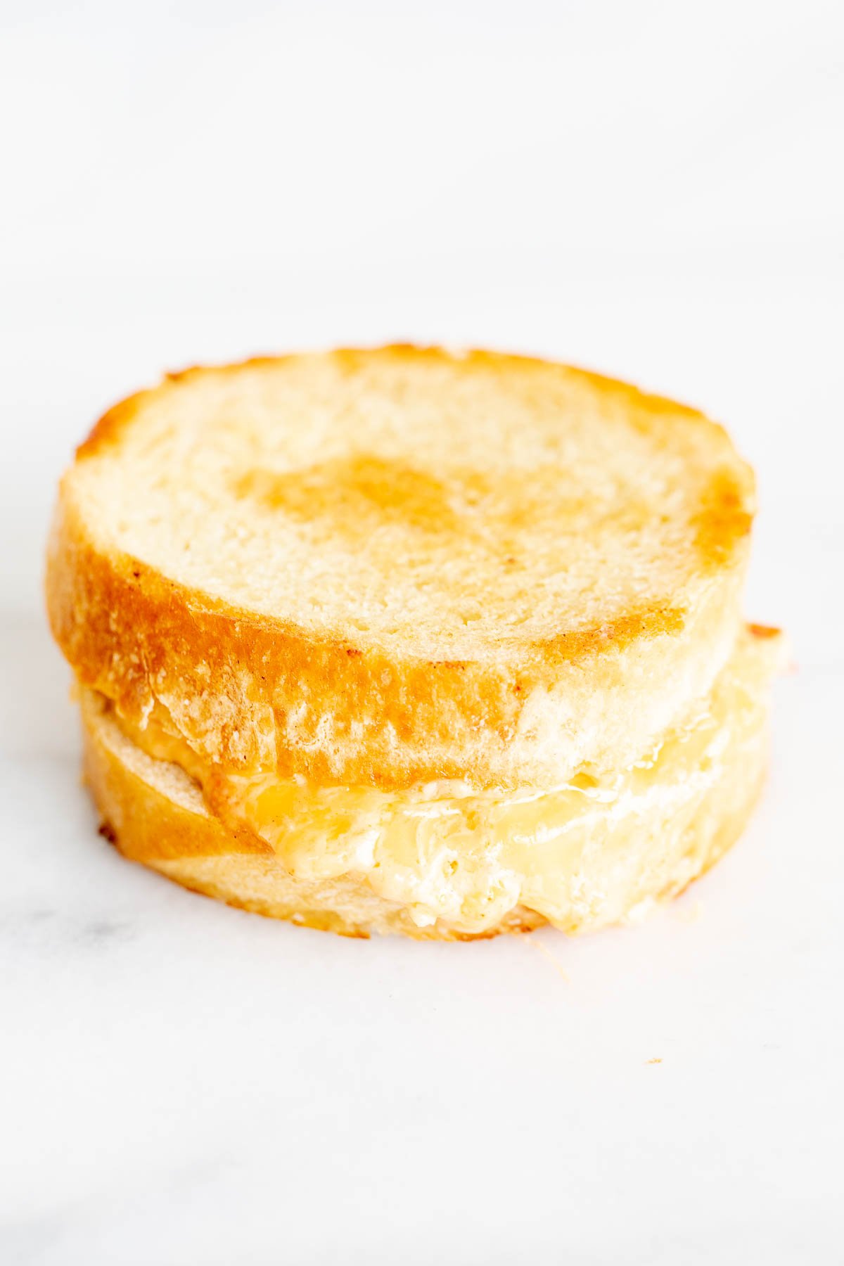 A pimento grilled cheese sandwich on round bread, on a marble countertop.