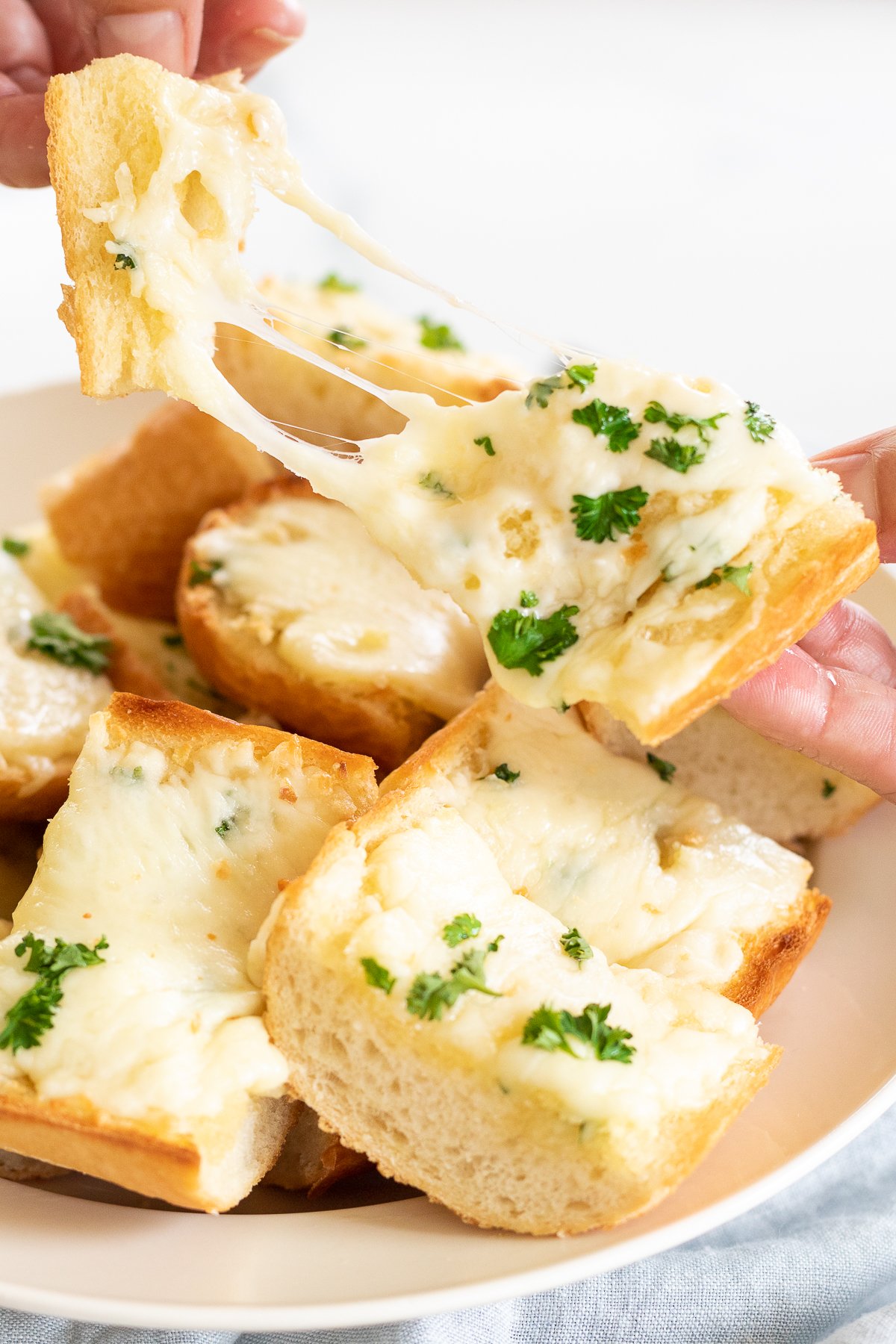 Garlic cheese bread in serving bowl, with hands pulling a piece apart to show cheese pull