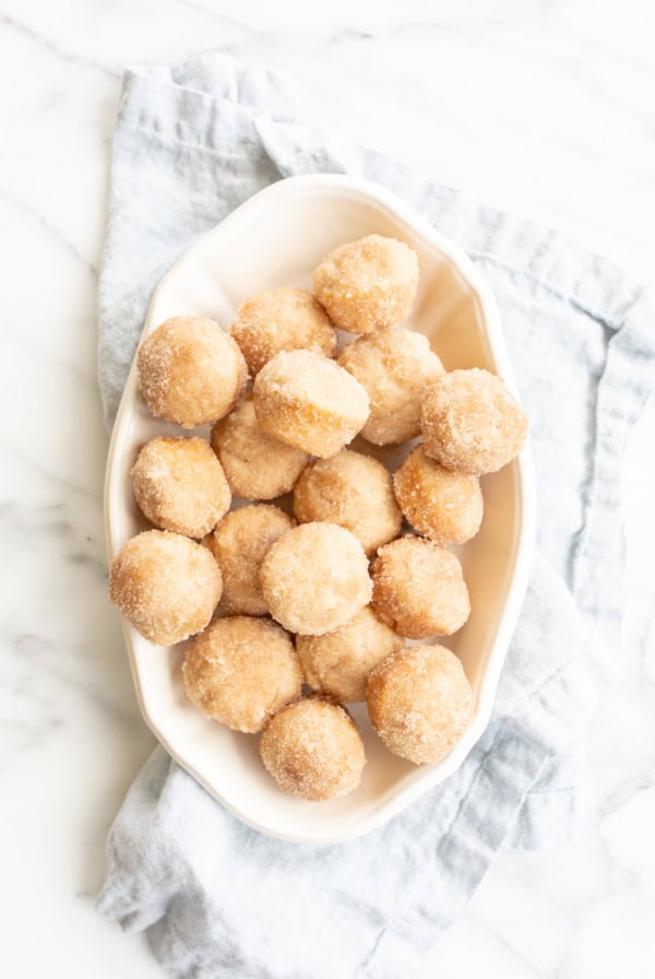 A white oval dish filled with sugar-coated muffins, placed on a light blue cloth on a marble surface.