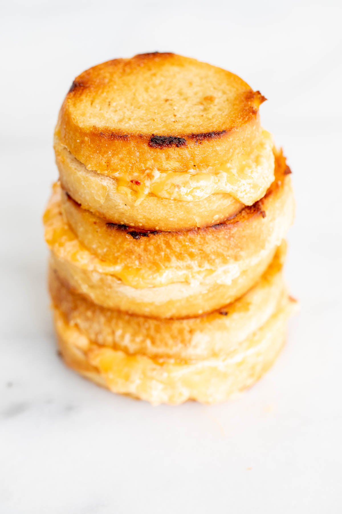 A stack of 3 pimento grilled cheese sandwiches on a marble countertop.