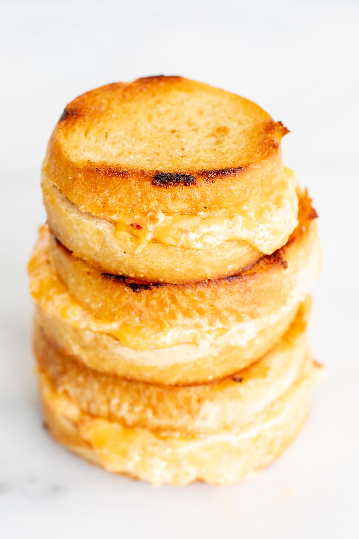 A stack of 3 pimento grilled cheese sandwiches on a marble countertop.