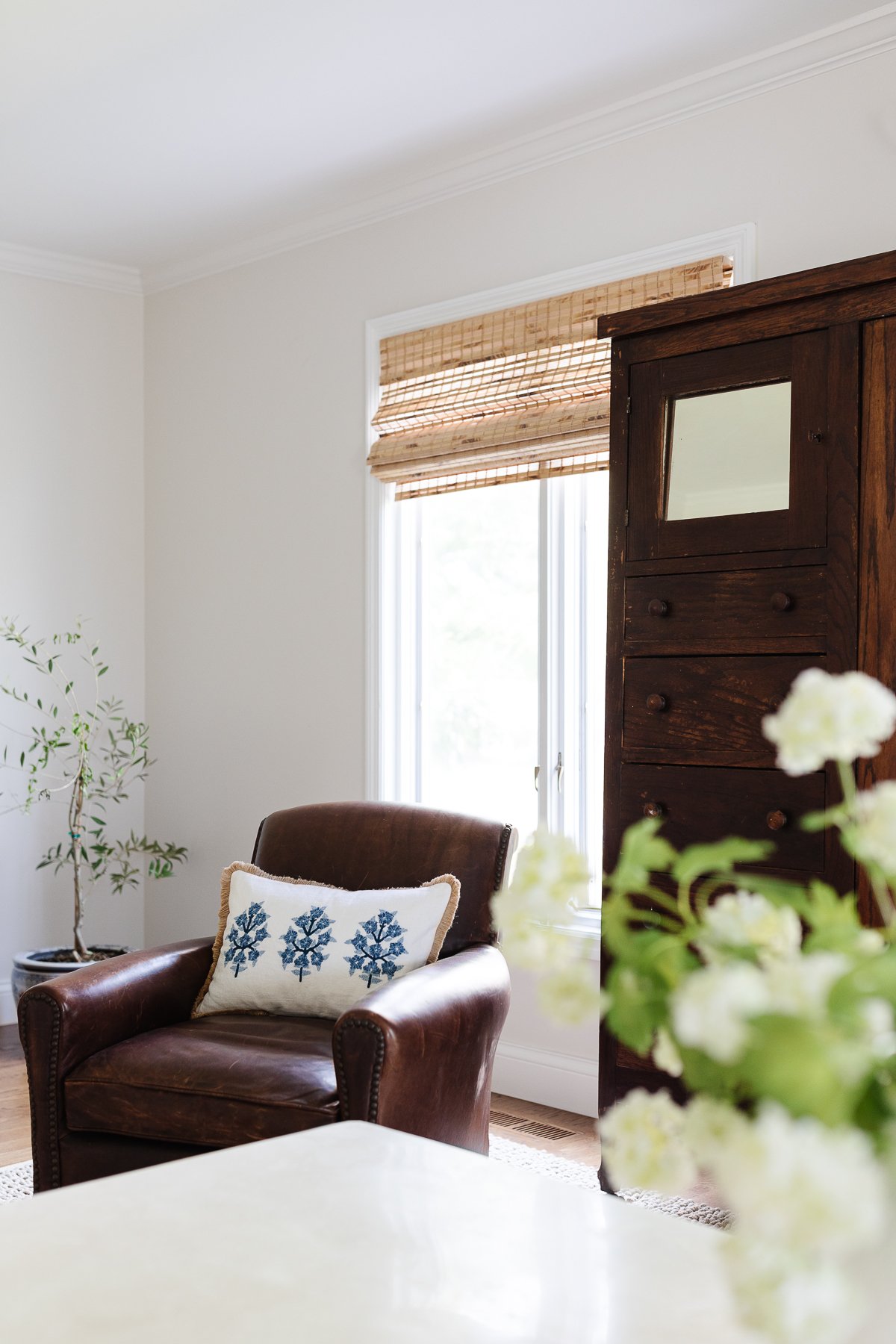 A family room with an antique armoire and bamboo blinds.