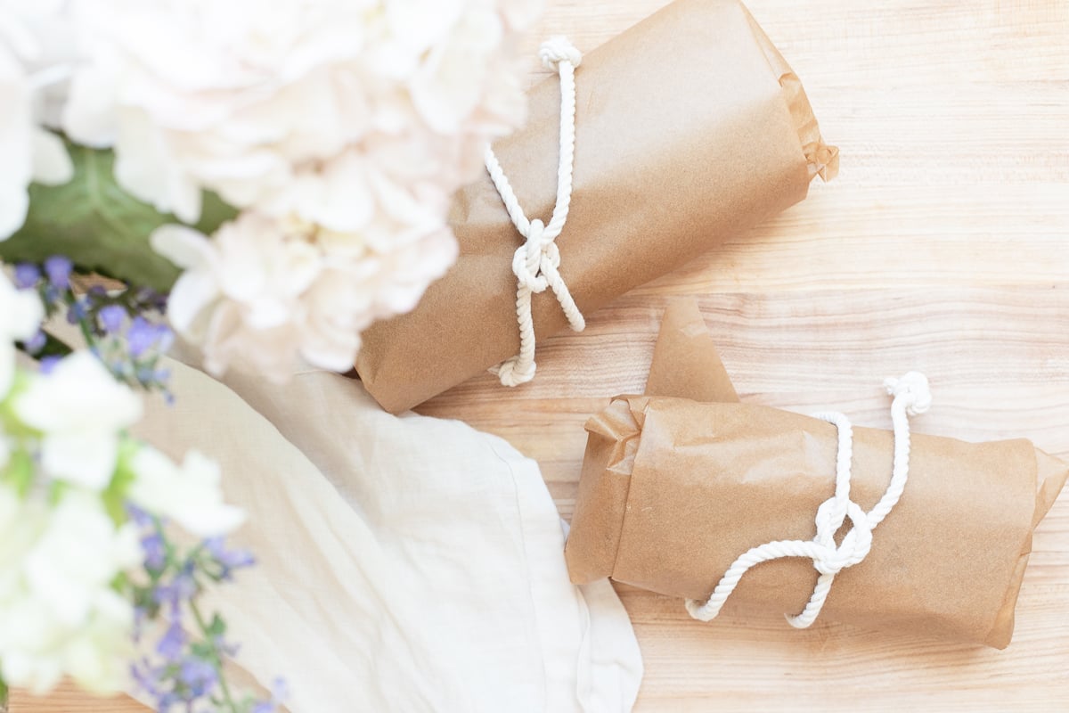 Picnic sandwiches on a wooden cutting board, wrapped in brown paper with a white string. 