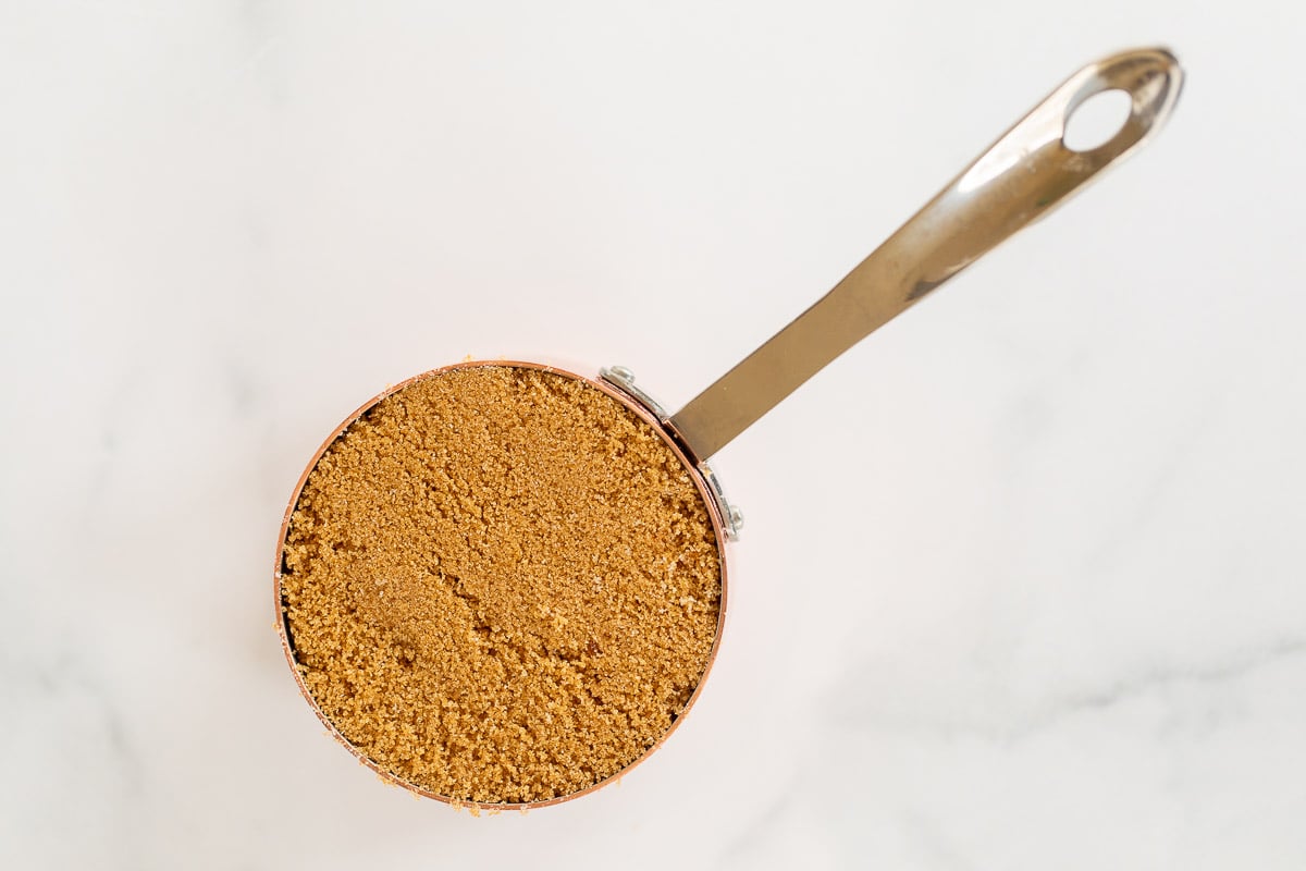 Dark brown sugar in a copper measuring cup on a marble countertop.