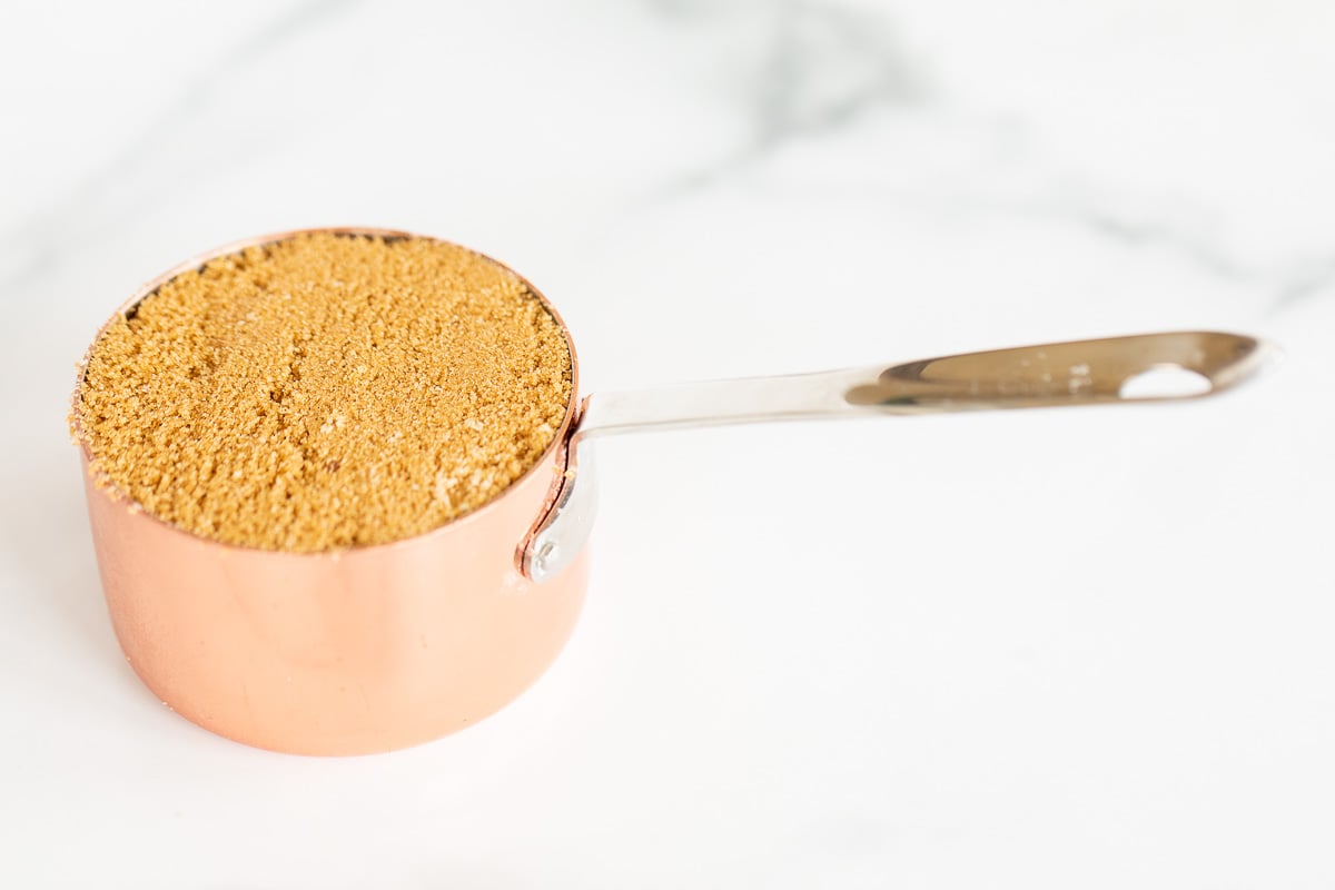 Light brown sugar in a copper measuring cup on a marble countertop.