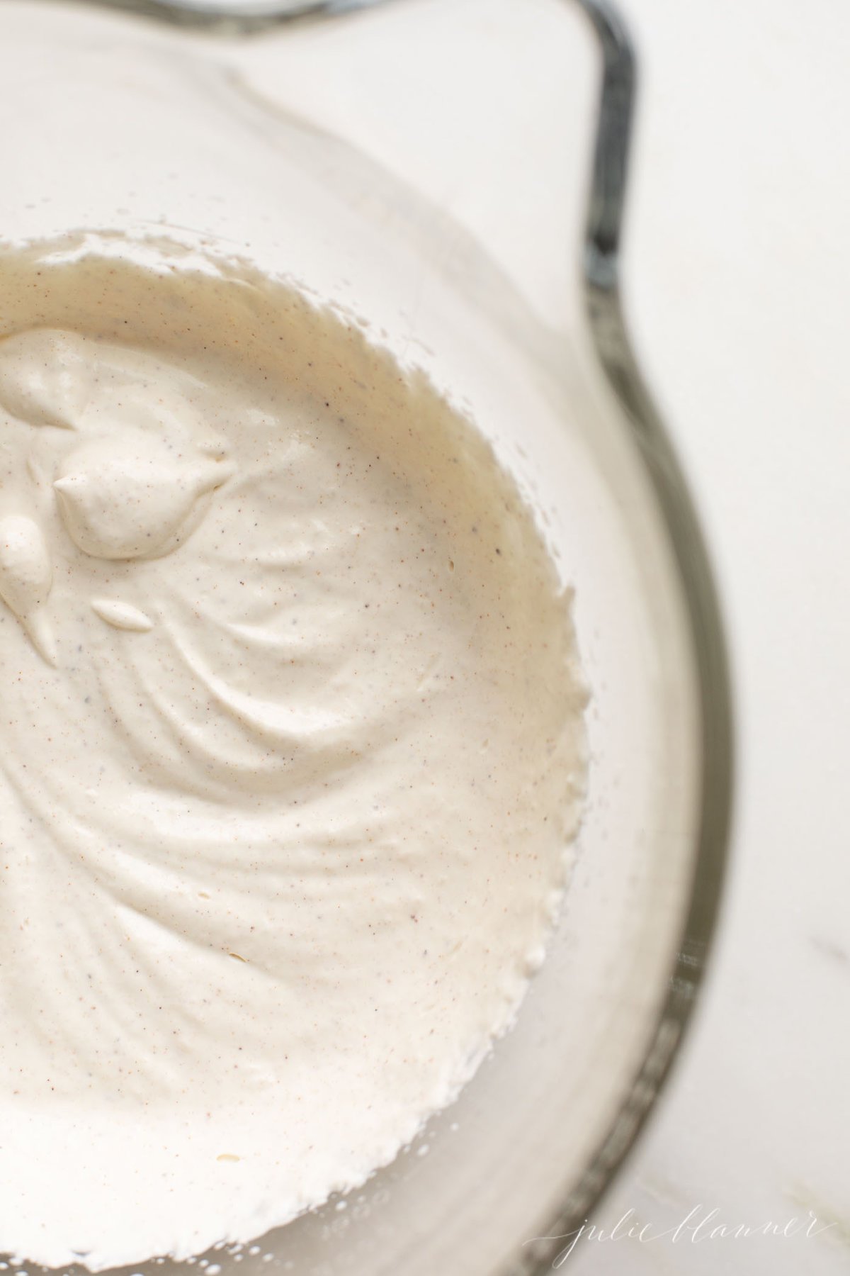 A clear glass mixing bowl of a stand mixer filled with whipped cream. 