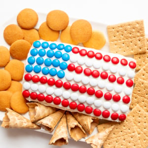 A red white and blue snack made of Funfetti dip in a flag shape, on a plate of cookies and crackers.