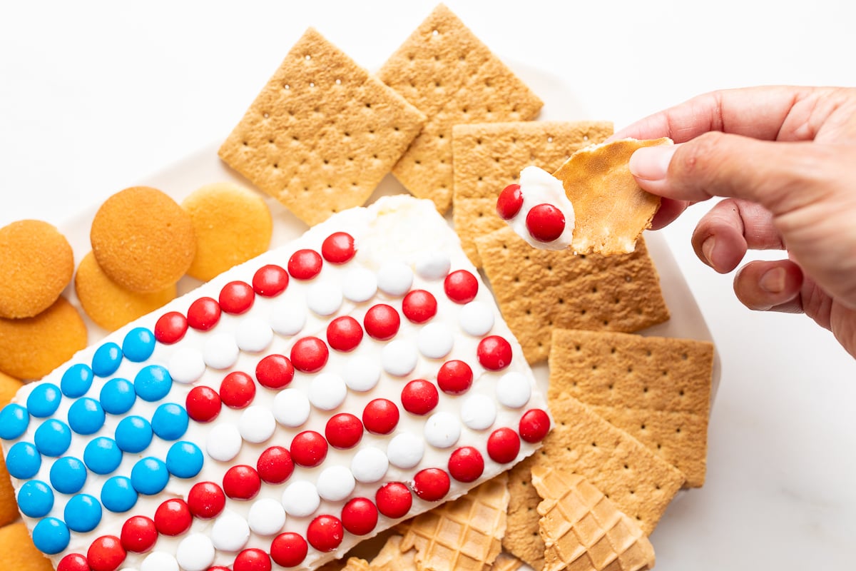 A red white and blue snack made of Funfetti dip in a flag shape, on a plate of cookies and crackers.