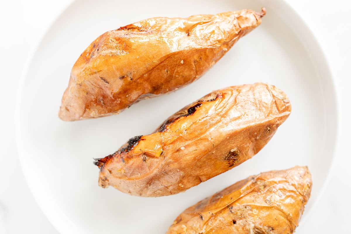 Three grilled sweet potatoes on a white plate.