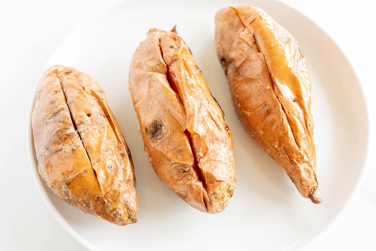 Three grilled sweet potatoes on a white plate.