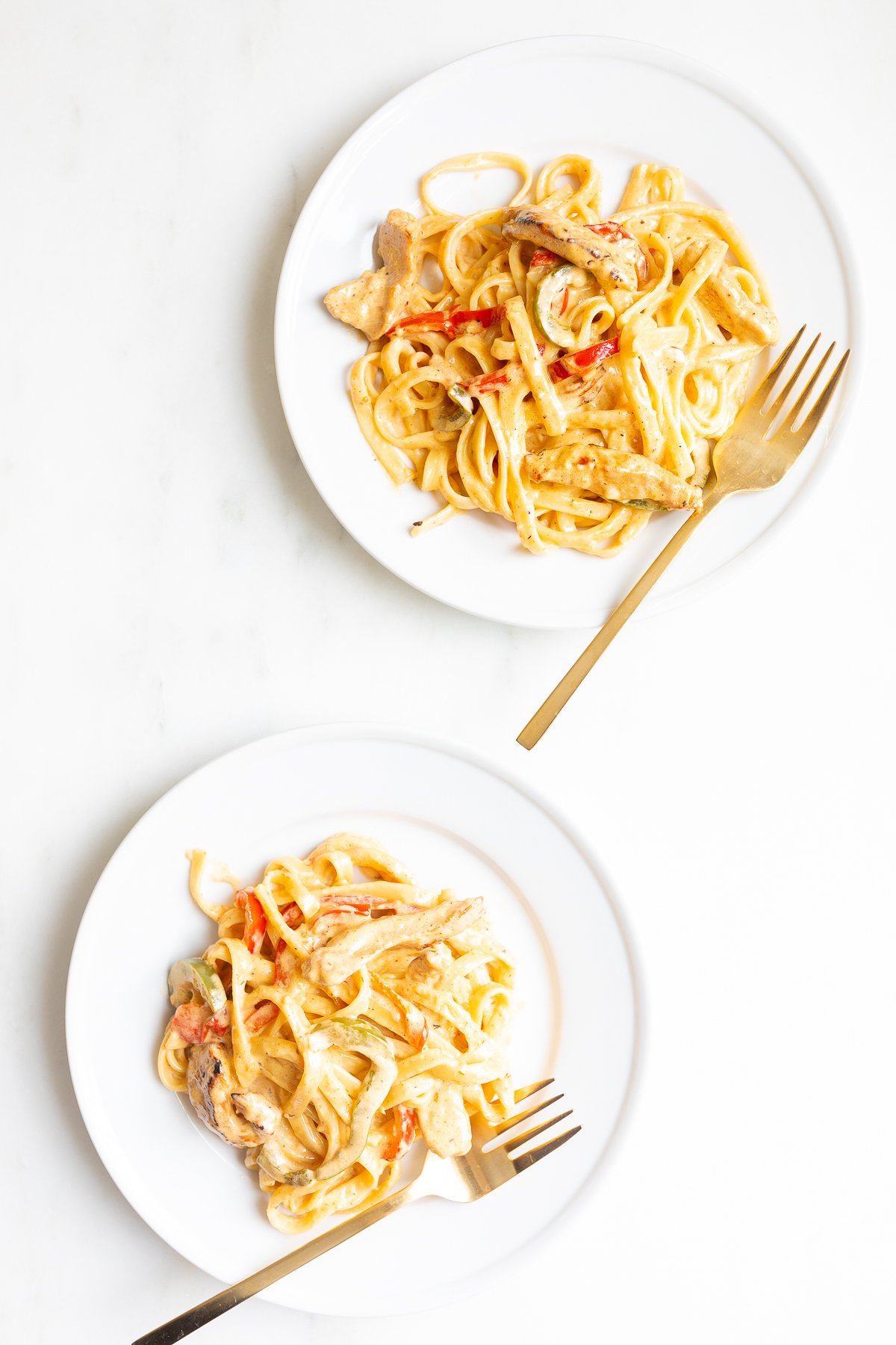 Two white plates of pasta, with gold forks.