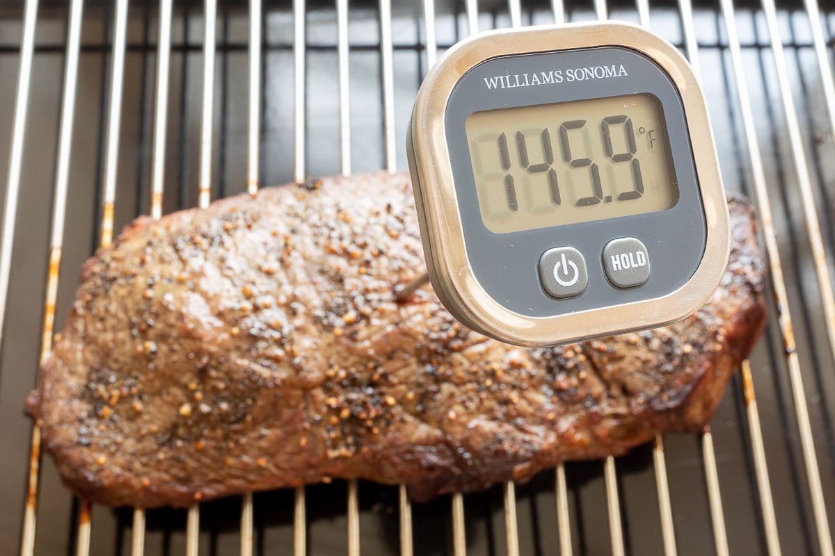 Instant read thermometer taking temperature of steak on grill