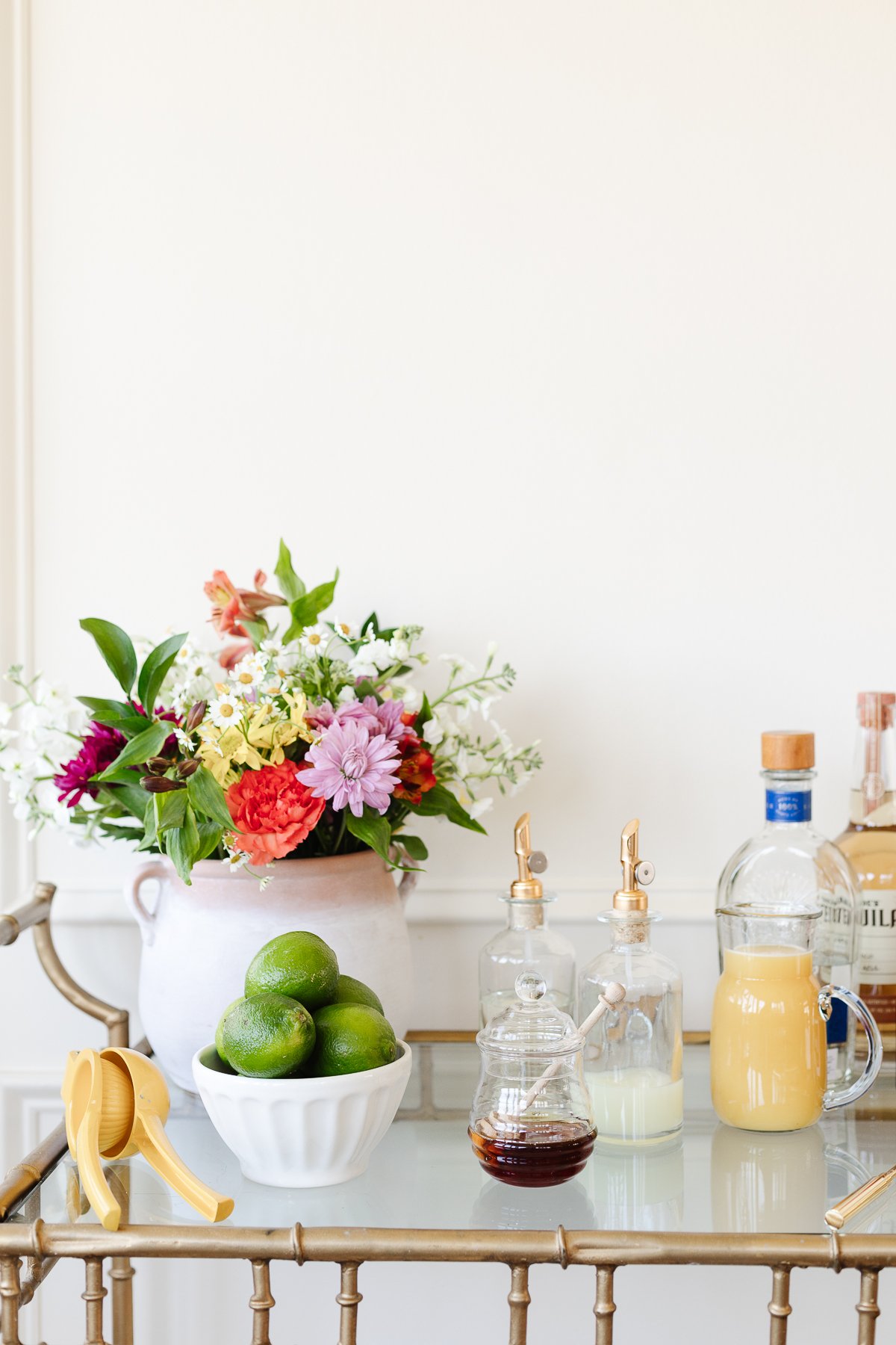 Bar cart set up with lemon squeezer, bowl of limes, flower arrangement, and cocktail accessories