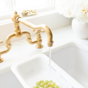 Over-the-sink strainer being used to rinse bunch of green grapes