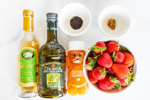 Various ingredients on a marble surface; includes vinegar, olive oil, honey and pepper to make a salad