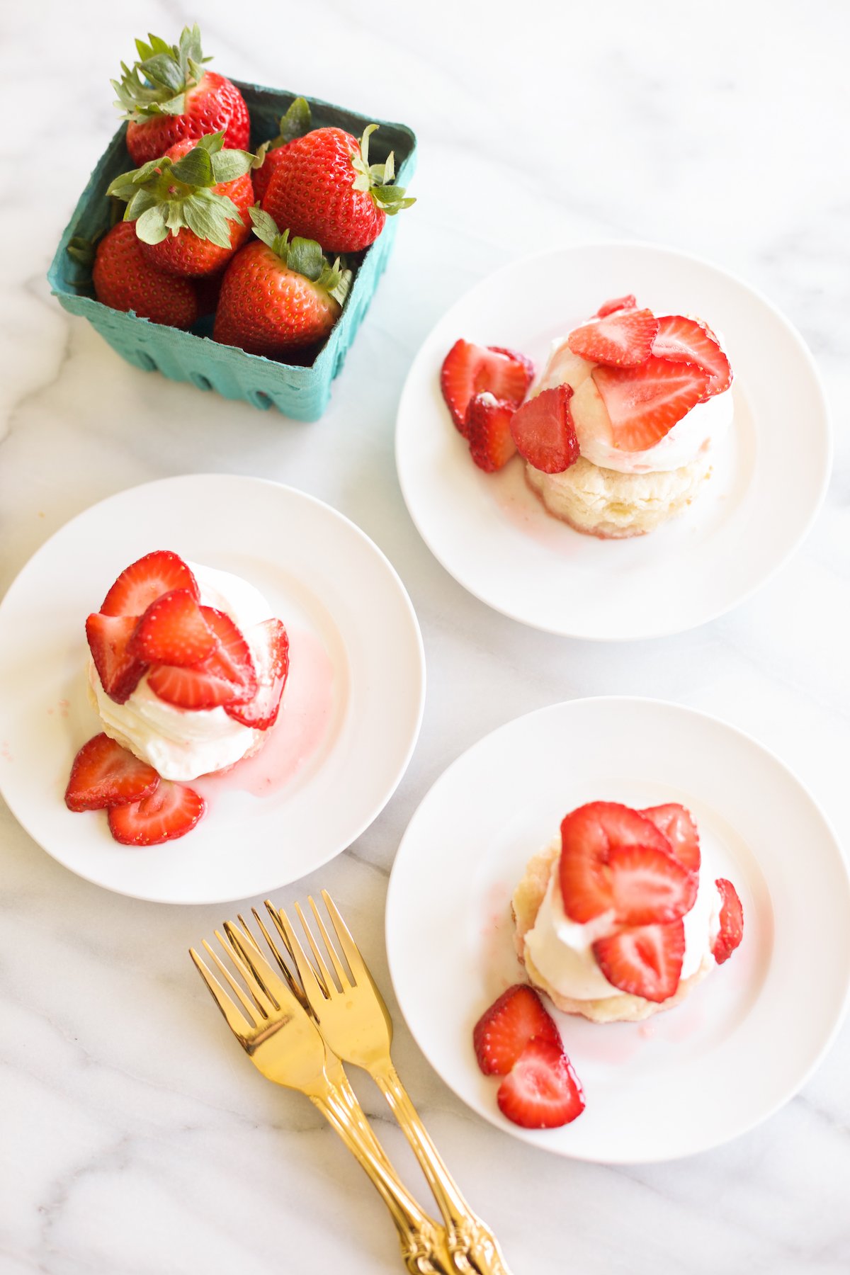 strawberry shortcake on a white plate, blue box of strawberries in background.