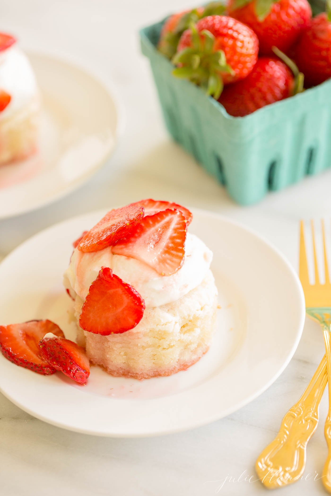strawberry shortcake on a white plate, blue box of strawberries in background.