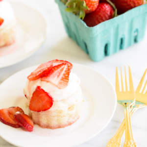 strawberry shortcake on a white plate, blue box of strawberries in background.