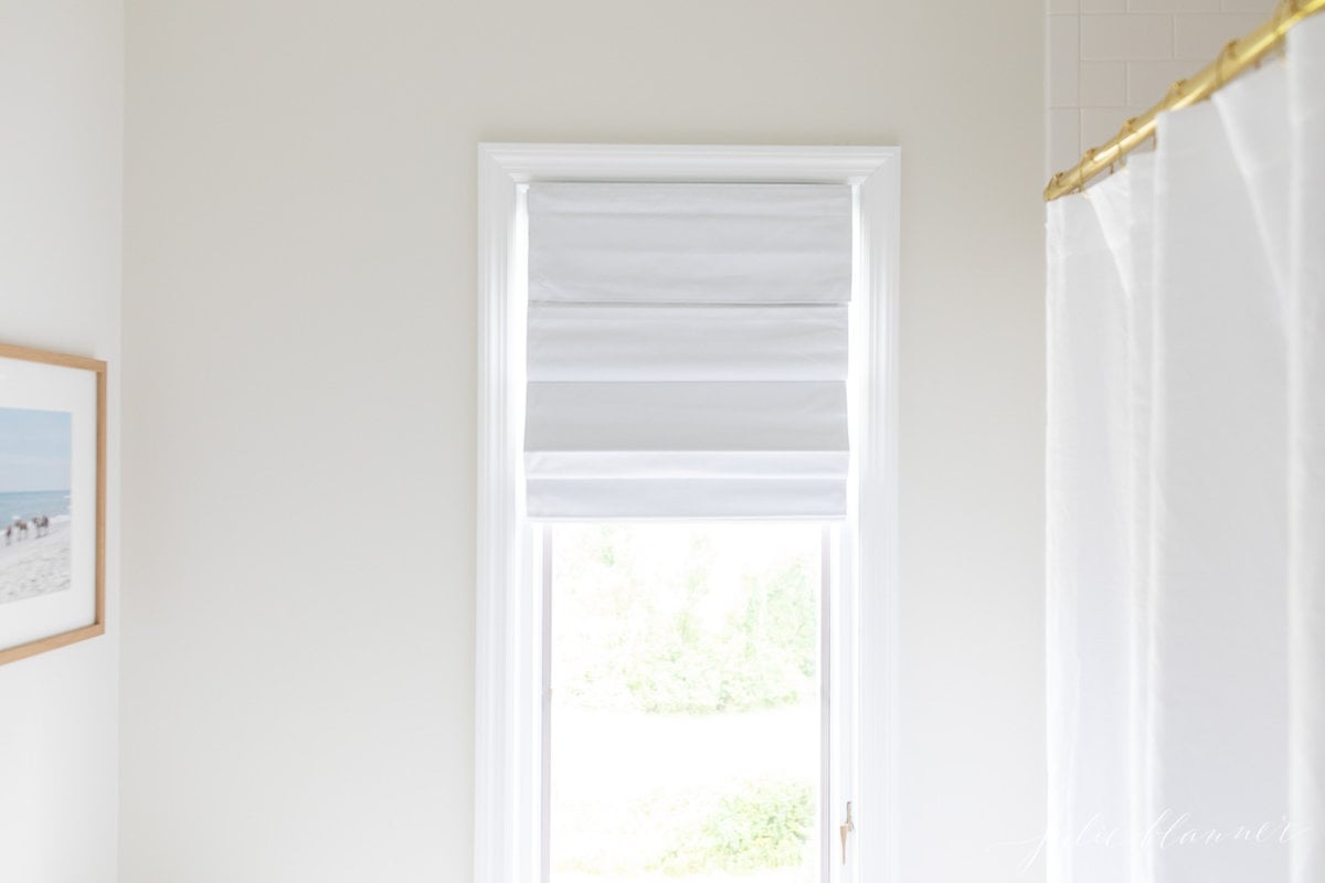 A white bathroom with white accessories and a brass shower curtain rod.