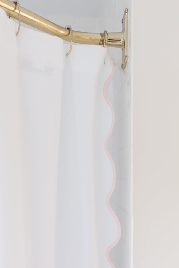 An unlacquered brass shower curtain rod with a white scalloped shower curtain.