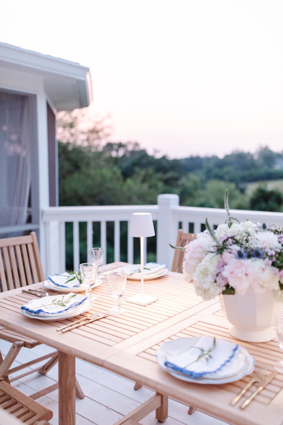 teak dining table with flowers, outdoor lamps and sunset view