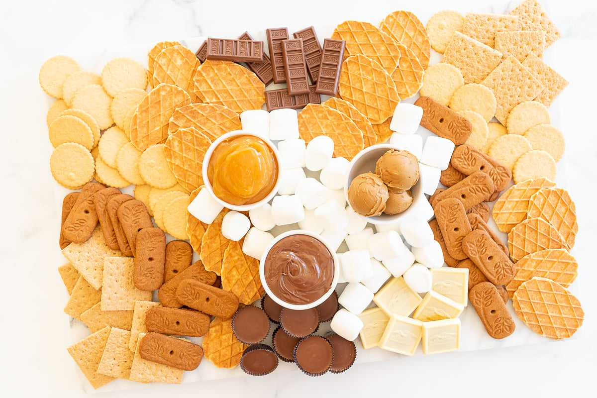 A s'mores charcuterie board filled with various marshmallows, cookies, crackers and dessert spreads.