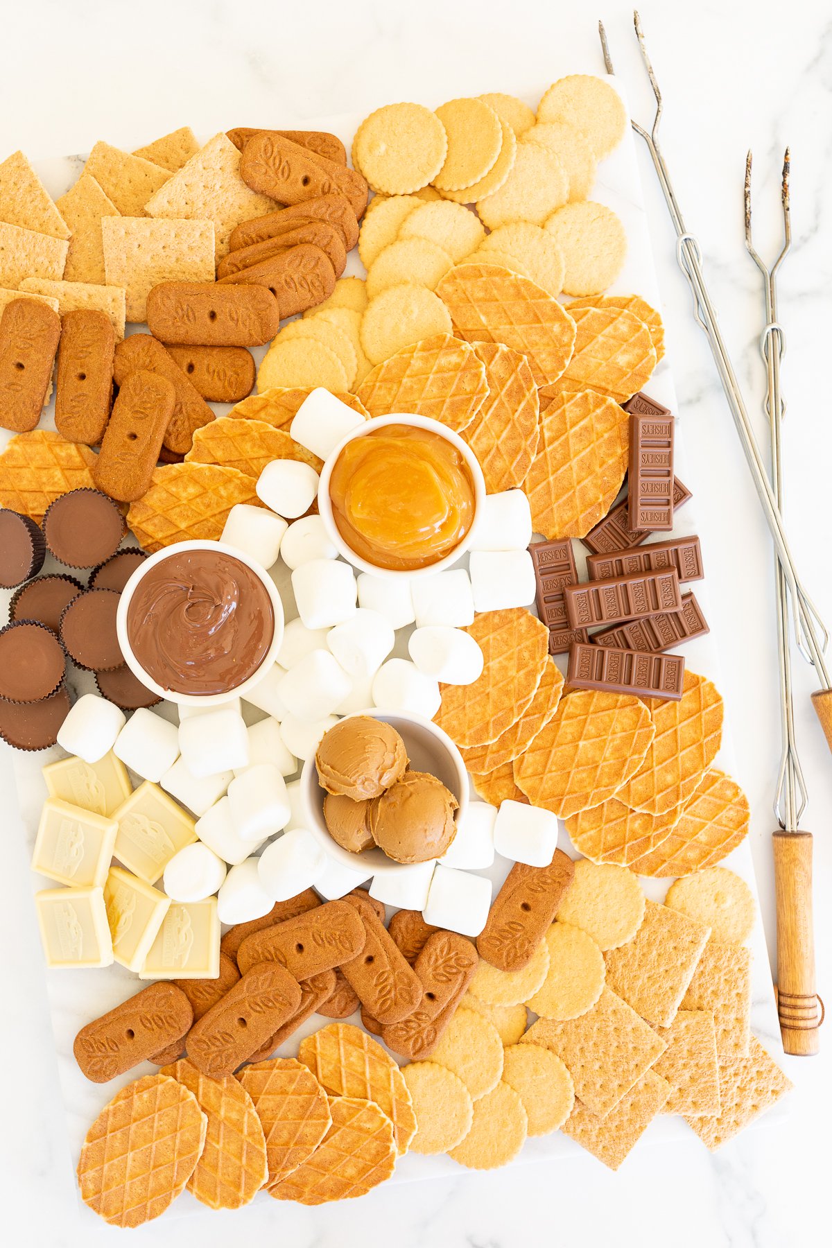 A s'mores charcuterie board filled with various marshmallows, cookies, crackers and dessert spreads.