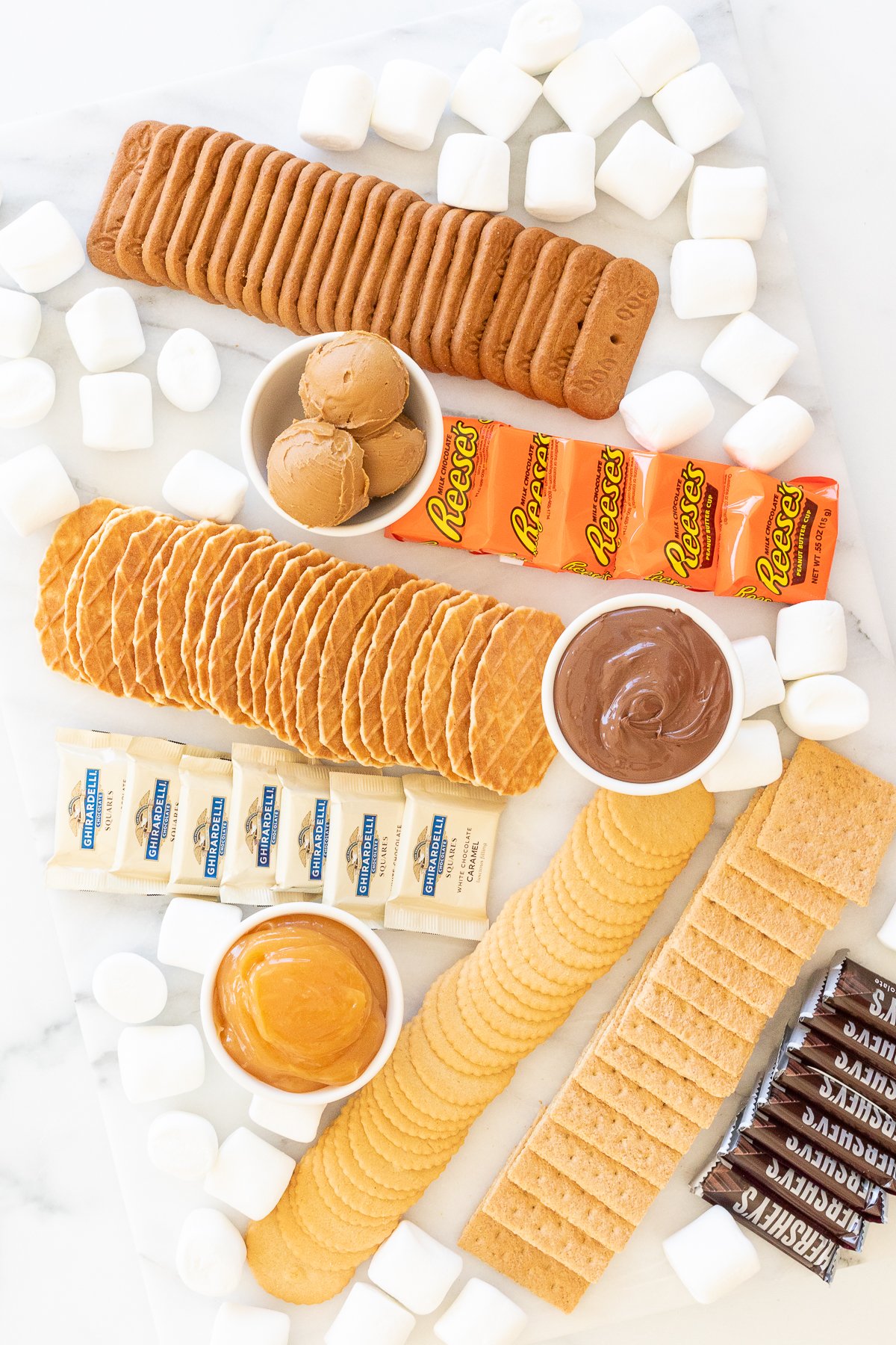 A smores charcuterie board filled with various marshmallows, cookies, crackers and dessert spreads.