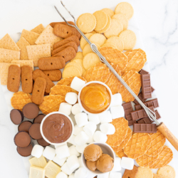 A smores charcuterie board filled with various marshmallows, cookies, crackers and dessert spreads.