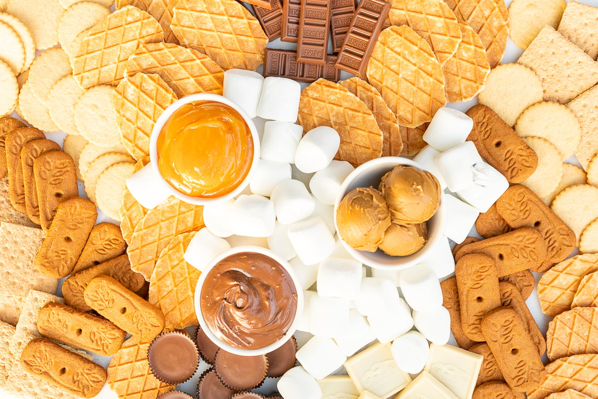 A s'mores board filled with various marshmallows, cookies, crackers and dessert spreads.