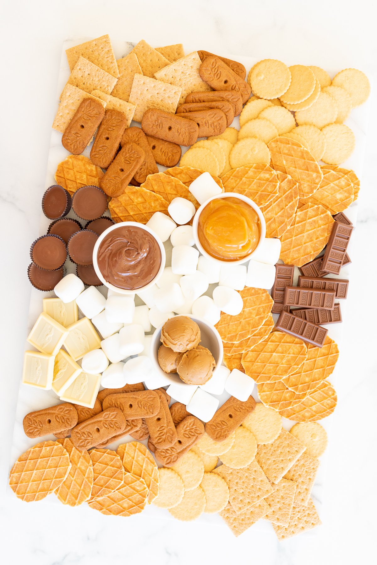 A smores charcuterie board filled with various marshmallows, cookies, crackers and dessert spreads.