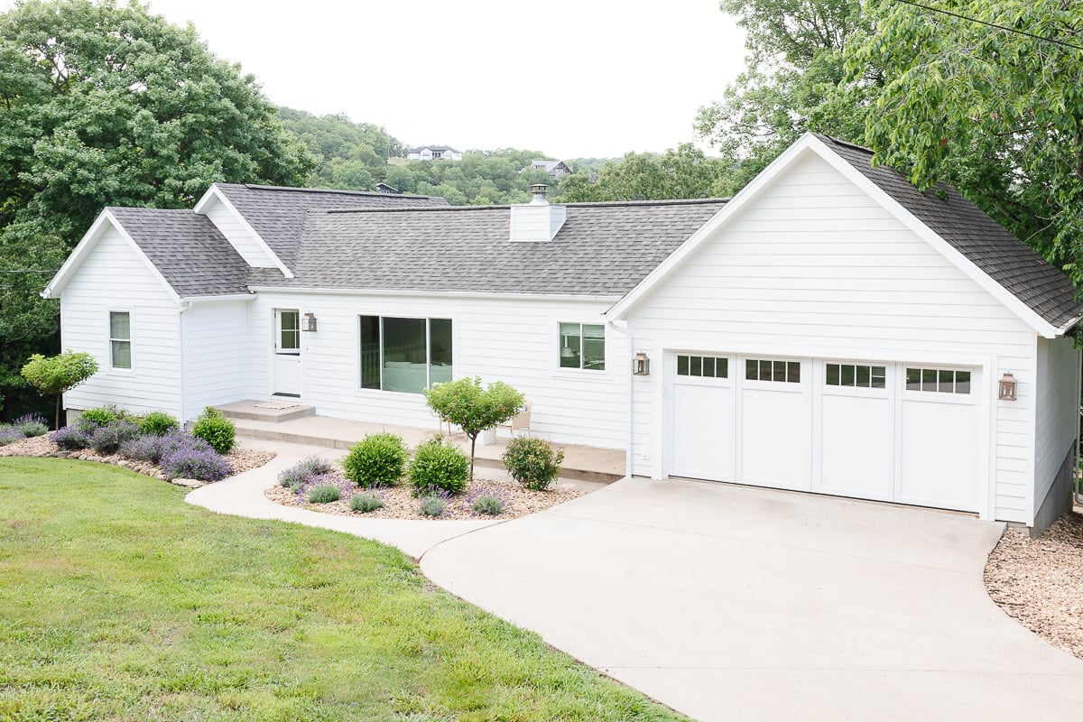 A white house with a gray roof and carriage garage doors.