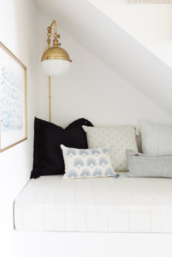 A reading nook under a staircase, upholstered with blue and white striped outdoor fabric