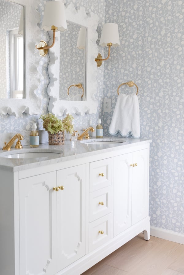 A soft blue and white wallpapered bathroom with a double white bathroom vanity.